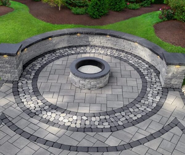 Circular fire pit patio built with BrookStone pavers, featuring contrasting gray tones and a cobble-style border.