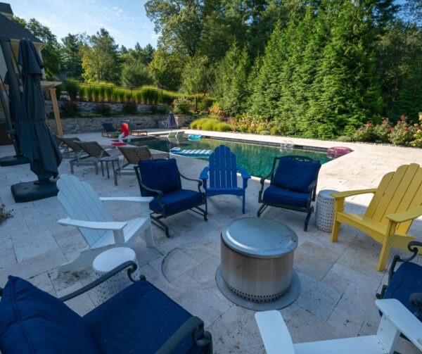 Outdoor seating area with modern chairs and fire table on Walnut French Pattern Travertine patio in Hopkinton backyard project by Elite Stoneworks.